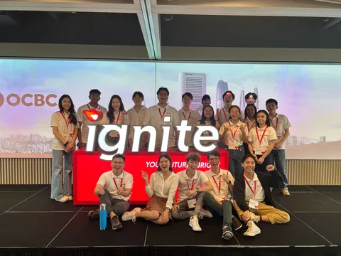 A group of people wearing white collared polo shirts and dark pants standing around a raised platform with the word "ignite" on it.
